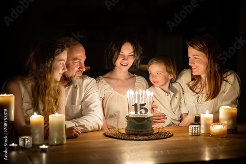 Cute fifteen years old girl making a wish before blowing candles on her birthday cake. Family of five celebrating childs birthday. photo