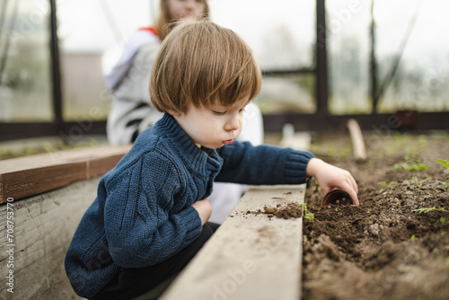 Cute toddler boy playing with soil on spring day. Kid planting a seedling in a greenhouse. Child exploring nature. Summer activities for kids.