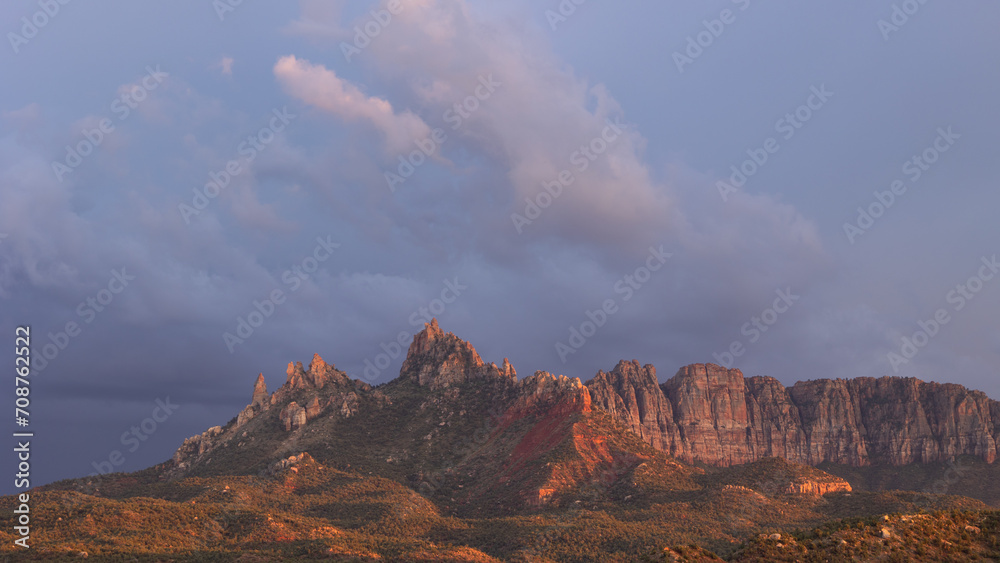 The rugged sandstone peaks of Eagle Crags near Zion Nat. park, Utah, USA catches the last of the sunset light as storm clouds drift past in the darkening sky.