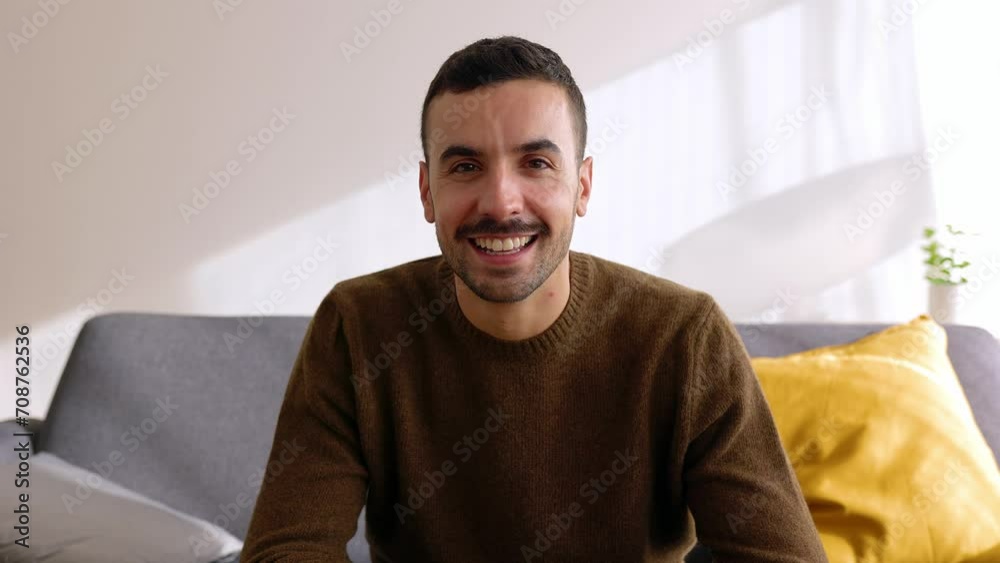 Portrait of young handsome adult man sitting on sofa at home. Joyful millennial guy in casual clothes relaxing on couch and smiling at camera.