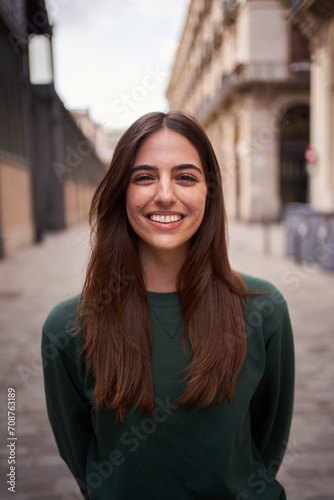 Vertical close up portrait joyful beautiful young Caucasian gen z woman happy smiling on street. Female people nice expression looking at camera in open air. Spanish girl posing for picture outdoor