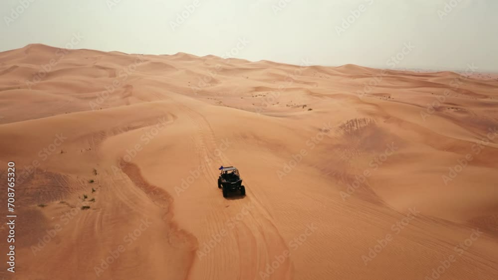 Tourist driving a dune buggy in Dubai desert dunes, aerial view on a hot summer day