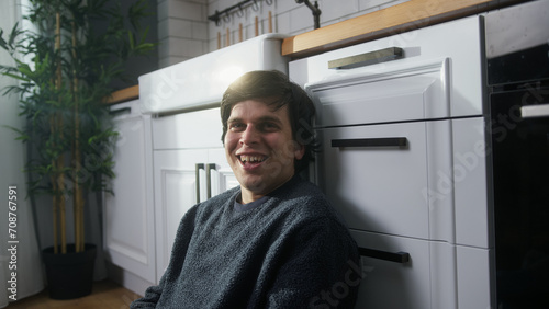 Portrait of smiling young man looking at camera and smiling in modern kitchen while sitting on the floor 