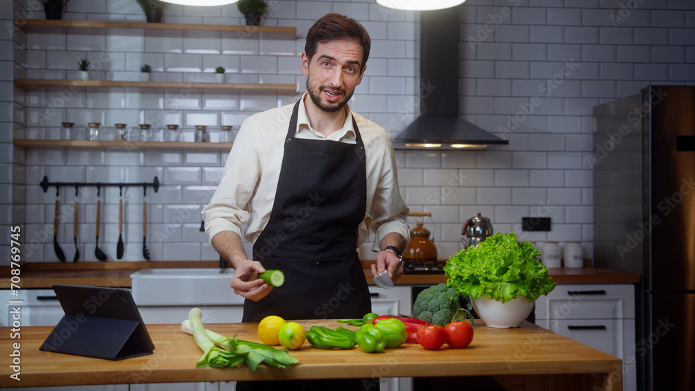 Bearded young vlogger man chef in an apron recording video cooking lesson about vegetarian meal in modern kitchen Bearded young vlogger man chef in an apron recording video cooking lesson about vegetarian meal in modern kitchen