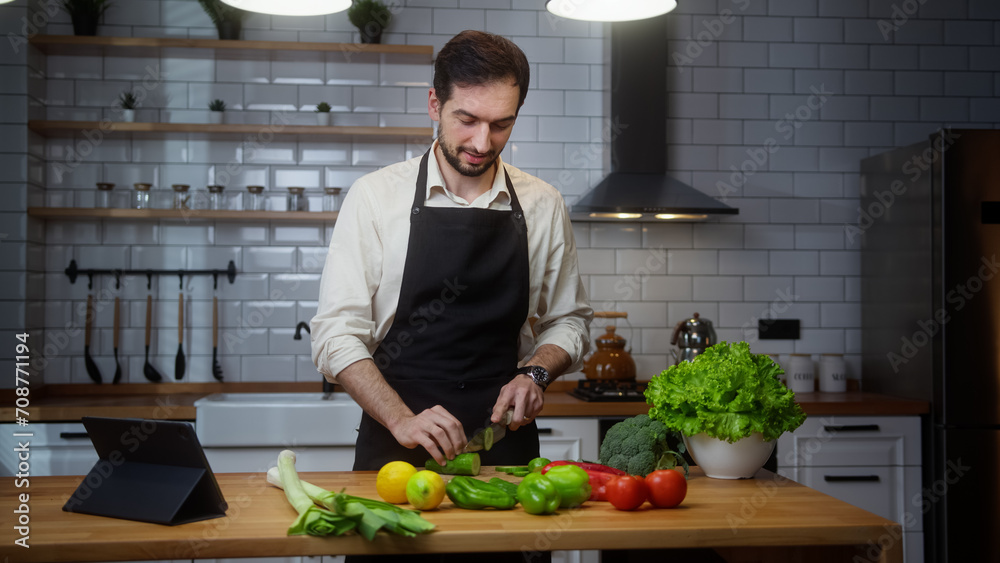 Fototapeta premium Vlogger professional man chef in an apron recording video cooking lesson about vegetarian meal in modern kitchen