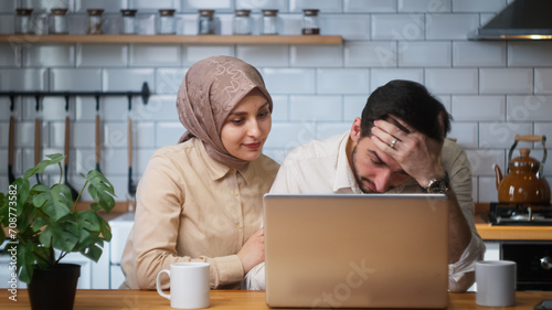 Photos Young married couple sitting in the kitchen using laptop saddened by the news, the loss, the wife consoles the husband