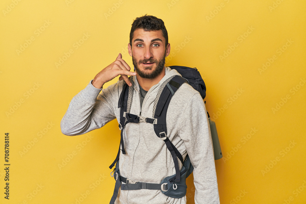 Young Hispanic man ready for hiking showing a mobile phone call gesture with fingers. Young Hispanic man ready for hiking showing a mobile phone call gesture with fingers.