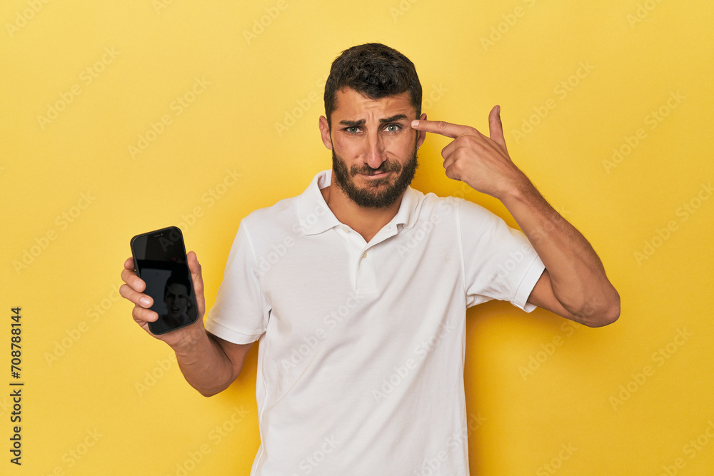 Young Hispanic man shows phone screen showing a disappointment gesture with forefinger. Young Hispanic man shows phone screen showing a disappointment gesture with forefinger.