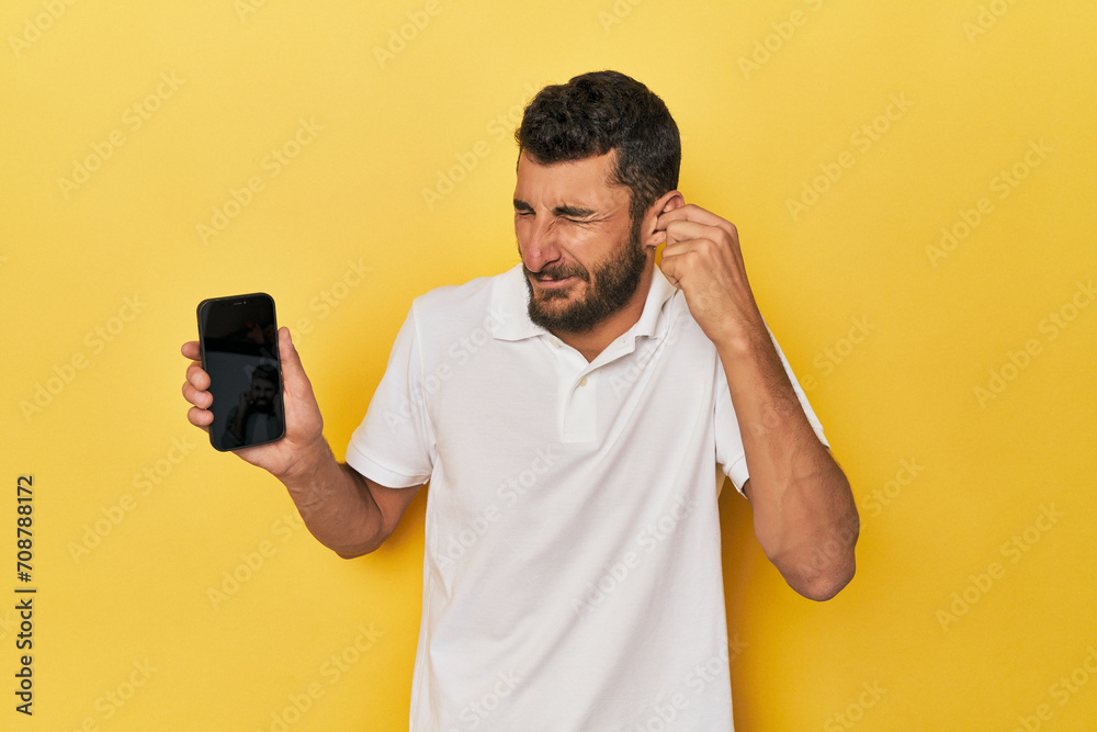 Young Hispanic man shows phone screen covering ears with hands. Young Hispanic man shows phone screen covering ears with hands.