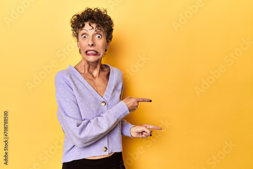 Mid-aged caucasian woman on vibrant yellow shocked pointing with index fingers to a copy space. photo