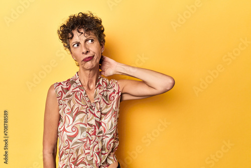 Fotografie Mid-aged caucasian woman on vibrant yellow touching back of head, thinking and making a choice