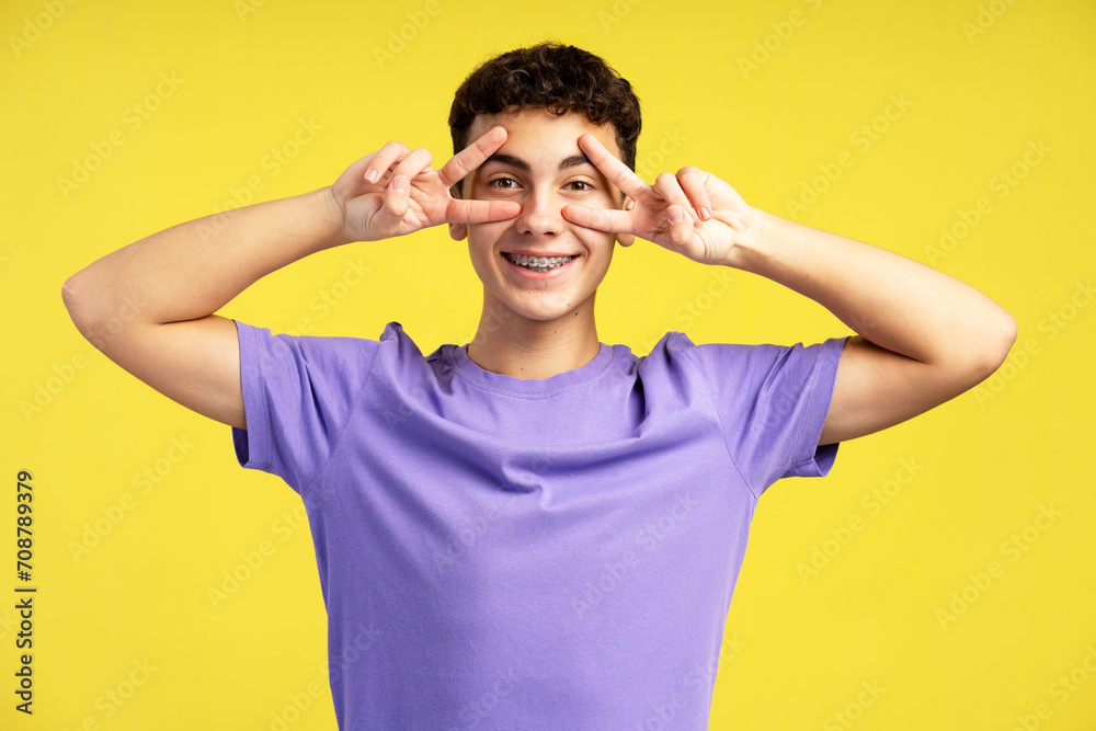 Smiling attractive boy, teenager wearing casual clothes gesturing, showing victory sign with fingers Smiling attractive boy, teenager wearing casual clothes gesturing, showing victory sign with fingers