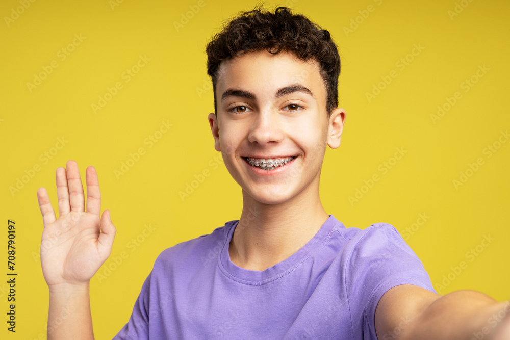 Portrait of excited teenage boy, influencer with dental braces waving hand, wearing purple t shirt Portrait of excited teenage boy, influencer with dental braces waving hand, wearing purple t shirt