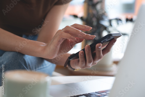 Close up, woman using mobile phone and laptop at coffee shop for online shopping, digital payment via mobile banking app, surfing the internet, social media connection photo