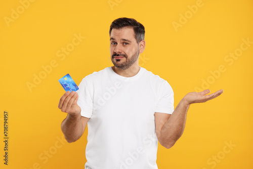 Confused man with credit card on orange background. Debt problem