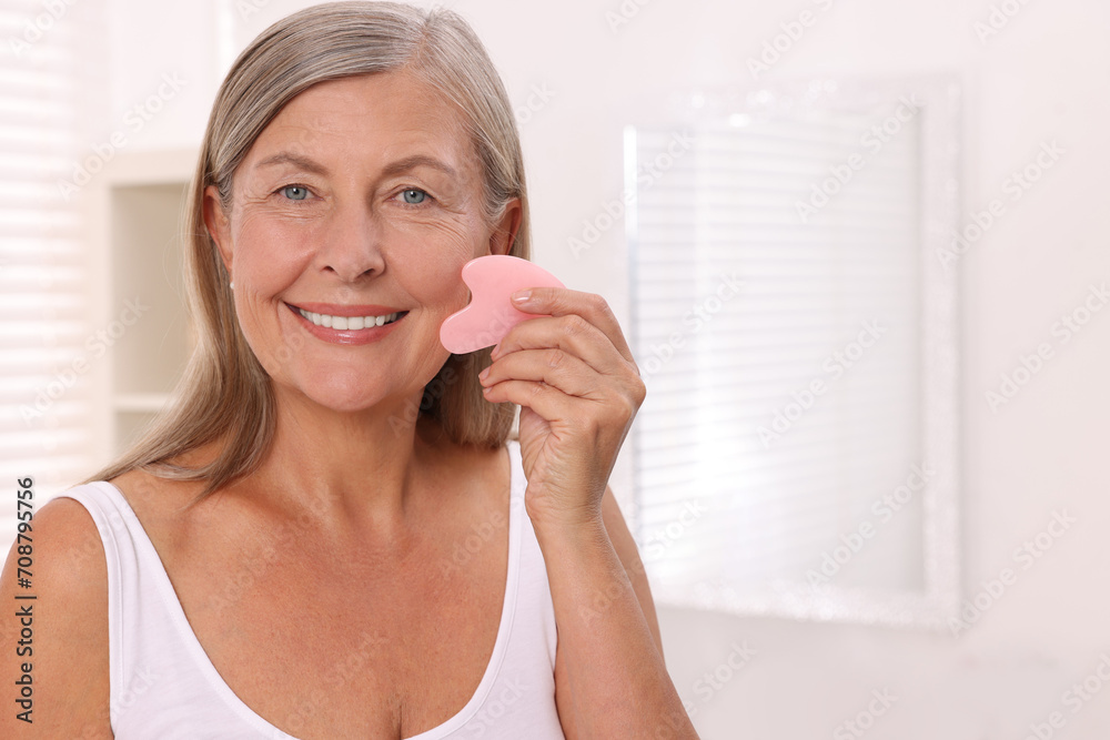 Woman massaging her face with rose quartz gua sha tool in bathroom. Space for text Woman massaging her face with rose quartz gua sha tool in bathroom. Space for text