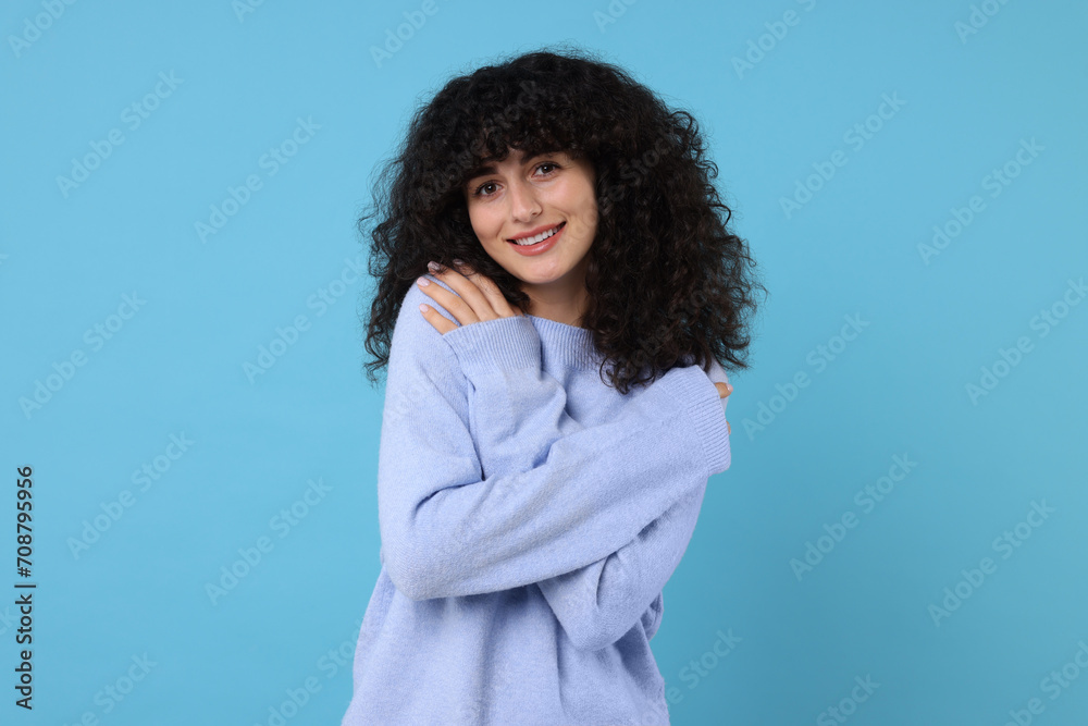 Happy young woman in stylish warm sweater on light blue background Happy young woman in stylish warm sweater on light blue background
