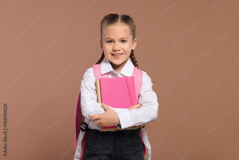 Happy schoolgirl with backpack and books on brown background Happy schoolgirl with backpack and books on brown background