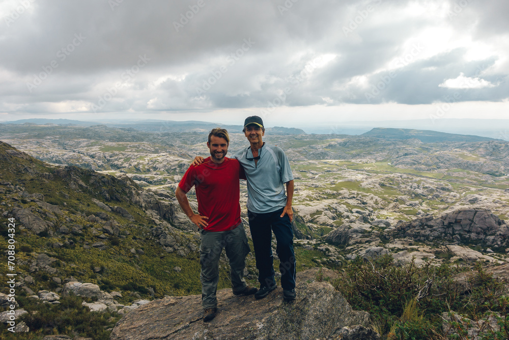 father and son pose in the top of a mountain with a really nice view
