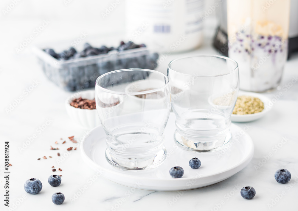 Empty glasses on a plate with ingredients to make a blueberry smoothie in behind Empty glasses on a plate with ingredients to make a blueberry smoothie in behind