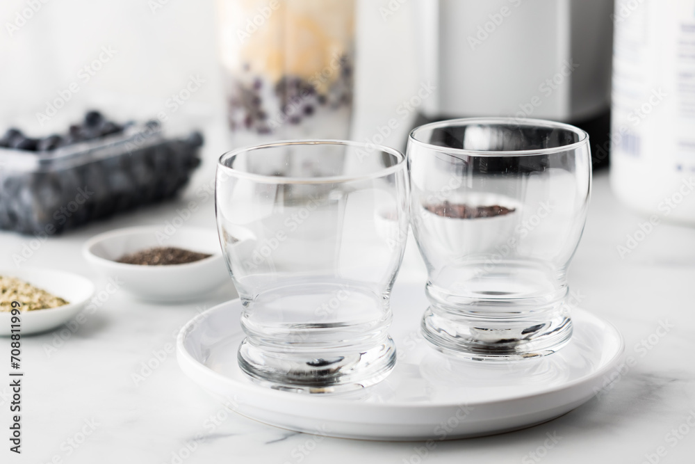 Empty glasses with Ingredients used to prepare a blueberry smoothie in behind. Empty glasses with Ingredients used to prepare a blueberry smoothie in behind.