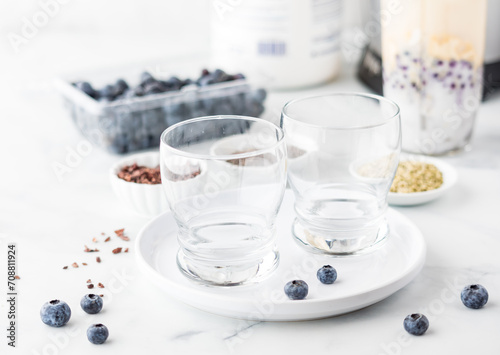 Empty glasses on a plate with ingredients to make a blueberry smoothie in behind