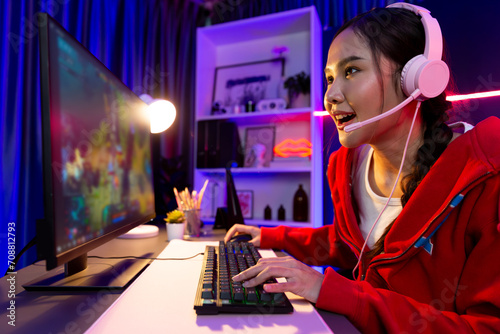 Host channel of young beautiful Asian gaming streamer playing fighting Moba at battle arena game on pc screen with multiplays, wearing pastel headphone at neon digital light modern room. Stratagem. photo