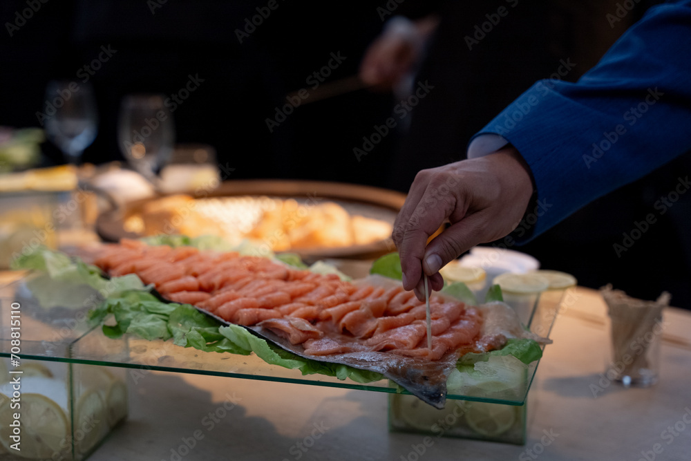 Mano en primer plano sirviendose salmón en una bandeja, rectangular