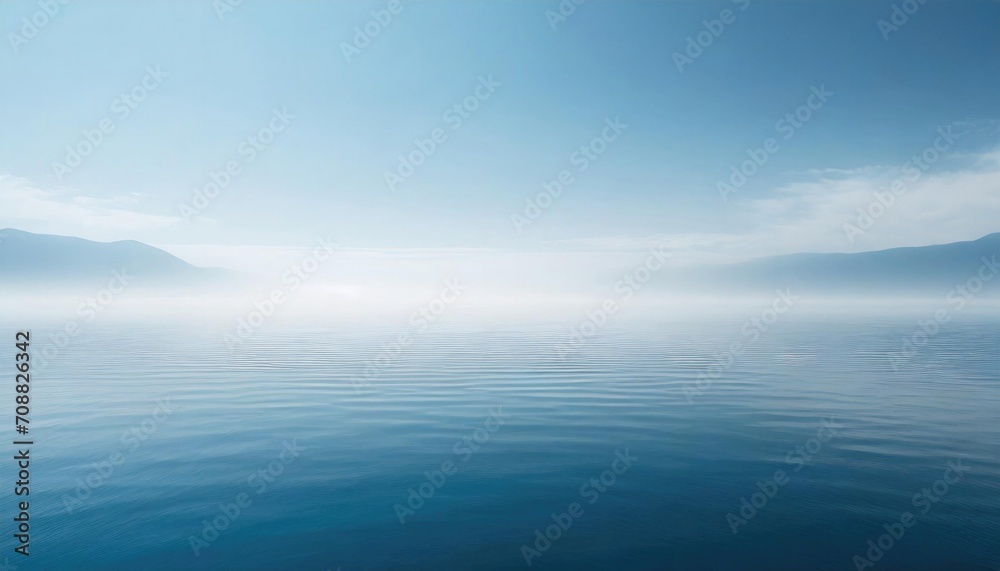 Fototapeta premium Serene seascape with a tranquil blue sea merging with a foggy sky and distant mountains.