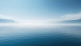 Serene seascape with a tranquil blue sea merging with a foggy sky and distant mountains.