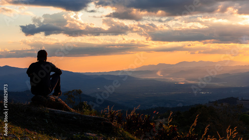 Silhouette of a man sitting on the rock waiting for sunset.