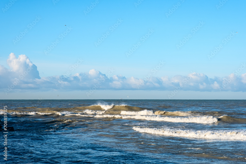 Sea surf against a background of white clouds in a blue sky