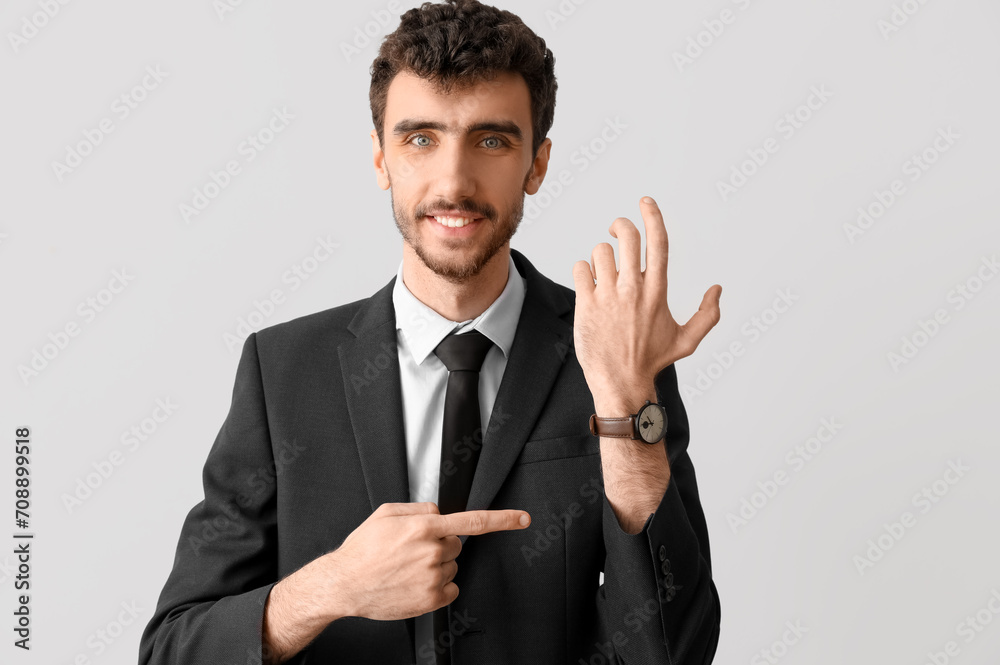 Young businessman in suit pointing at wristwatch on light background Young businessman in suit pointing at wristwatch on light background