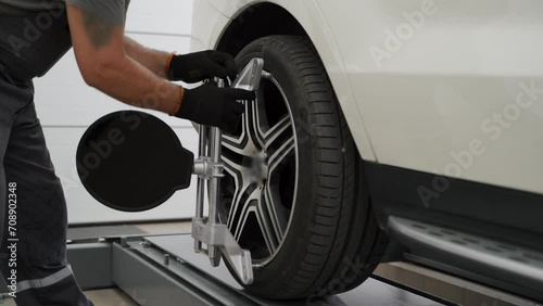 Mechanic adjusts wheel alignment on car at auto repair shop. Professional uses alignment equipment on tire for precise calibration. Vehicle maintenance, safety check, and service procedure. photo