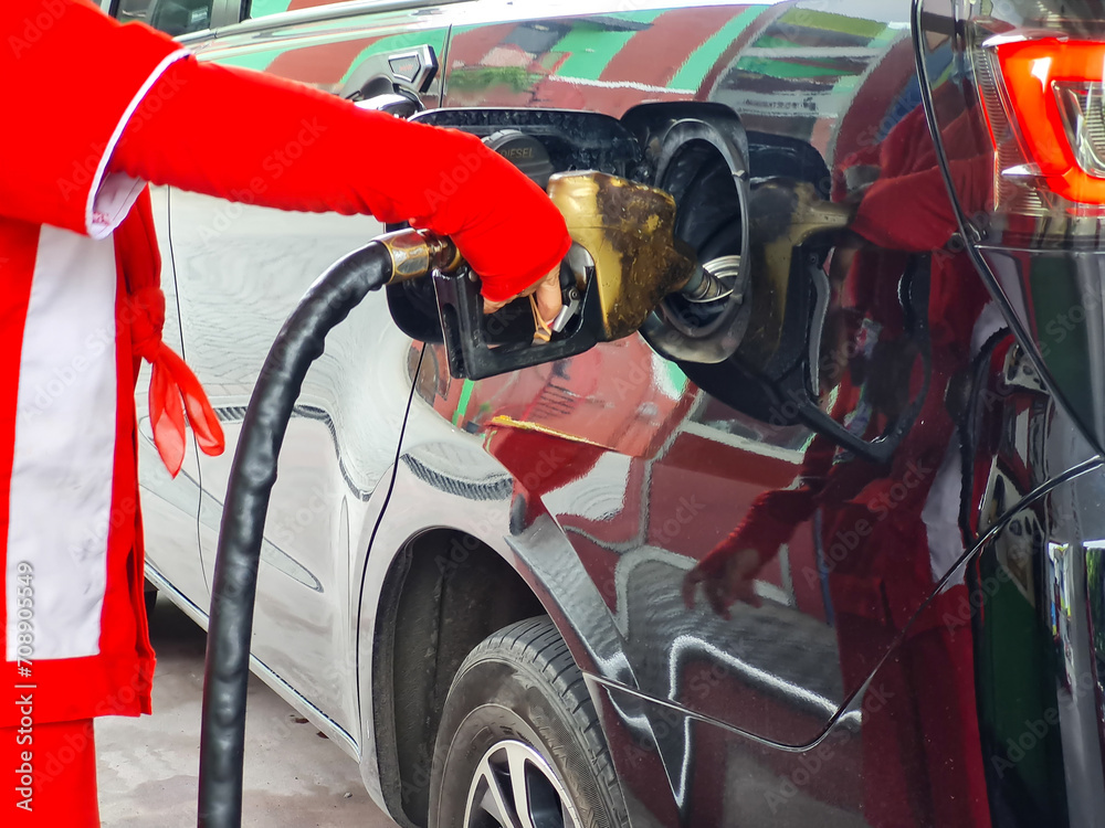 gas station worker's hand in red uniform holding fuel pump nozzle and refueling in diesel car. biodiesel fuel in Indonesia