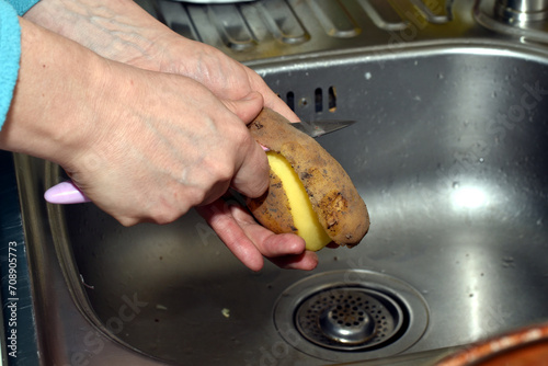 A woman peels potatoes with a knife.