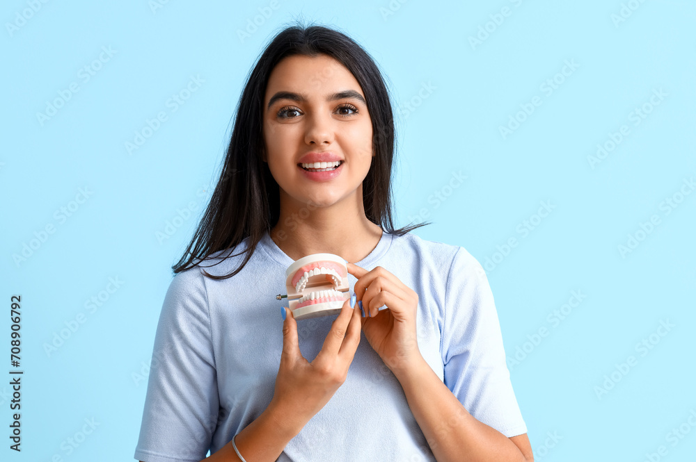 Smiling young woman with jaw model on blue background