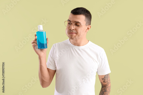 Handsome young man with bottle of mouthwash on green background. Dental care concept