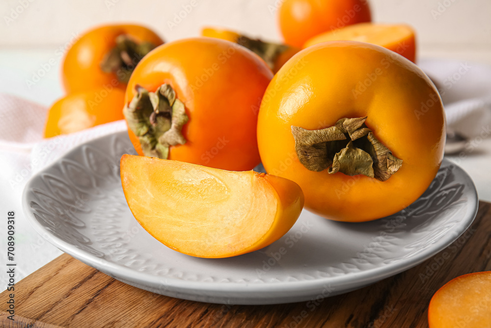 Plate with ripe persimmons on white background