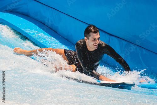 Young man surfing on a wave simulator at a water amusement park © romaset