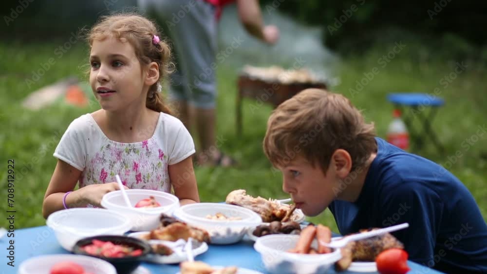 Boy and girl eat chicken, sausages with vegetables at picnic Boy and girl eat chicken, sausages with vegetables at picnic
