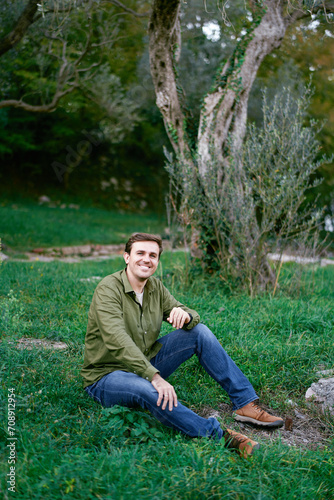 Young man sitting on green grass near the tree