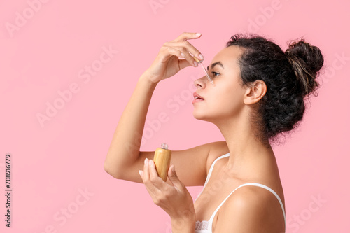 Beautiful young African-American woman with bottle of cosmetic oil on pink background