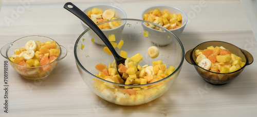 Owoce pokrojone na kawałki jak banan, pomarańcza i ananas nakładane do miseczek, dużo owoców poporcjowanych na posiłki 