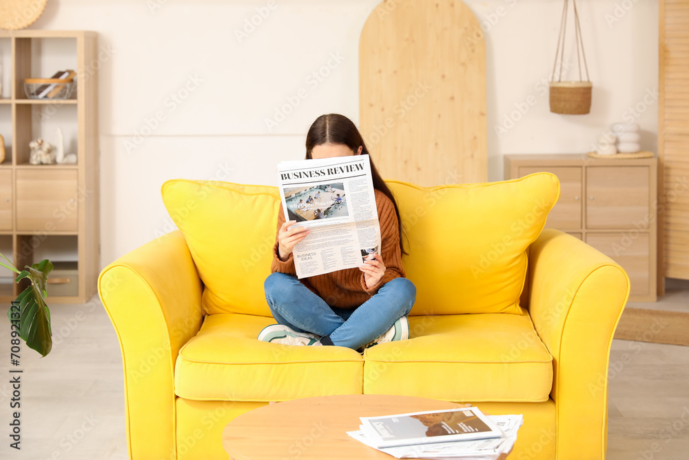 Young woman reading newspaper on sofa at home