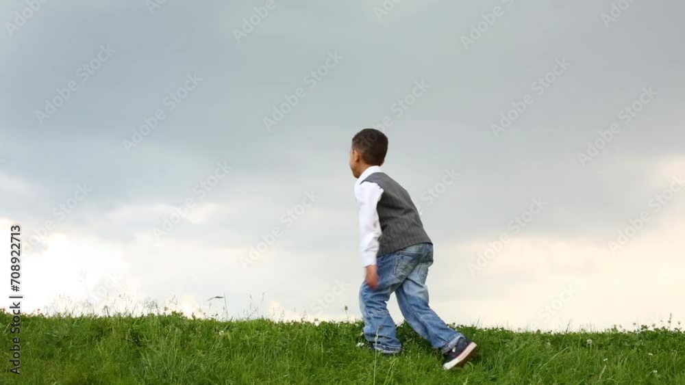 Cute boy in jeans walks and runs on green meadow at dull day Cute boy in jeans walks and runs on green meadow at dull day