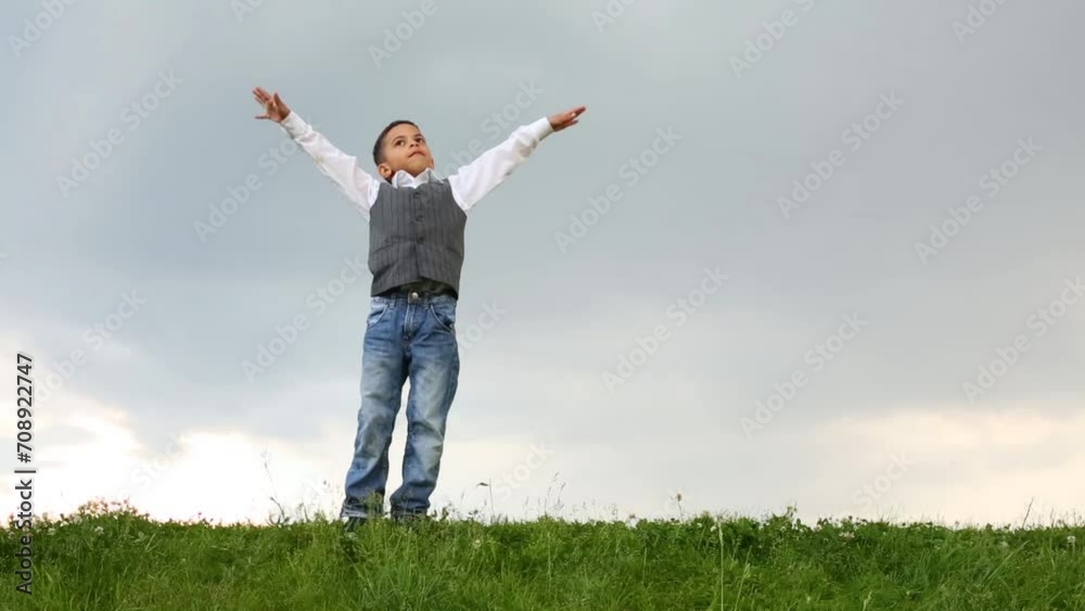 Cute boy in jeans raises his hands on green meadow at dull day Cute boy in jeans raises his hands on green meadow at dull day
