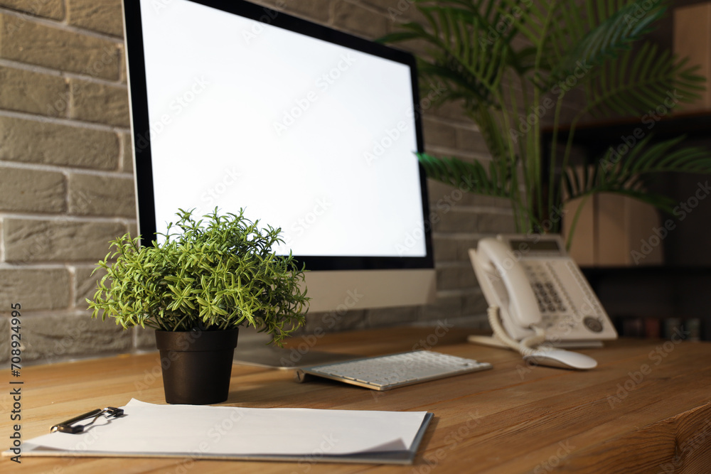 Blank computer monitor with flowerpot and clipboard on table in office at night, closeup Blank computer monitor with flowerpot and clipboard on table in office at night, closeup
