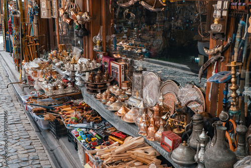 Vintage wooden spoons, aluminum jugs, retro knives, walking sticks, toy cars, retro lanterns, copper plates, hookah, rosary, ornaments and other stuff on the countertop of an antique shop. 