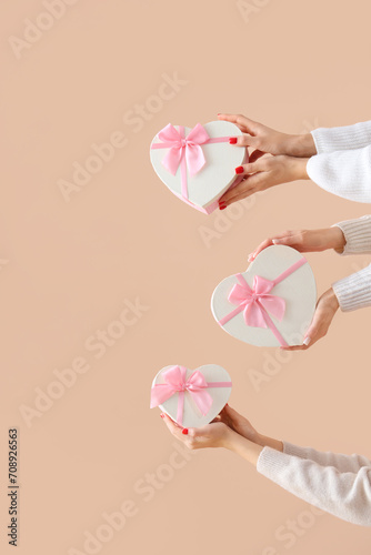 Female hands holding heart-shaped gift boxes on beige background. Valentine's Day celebration